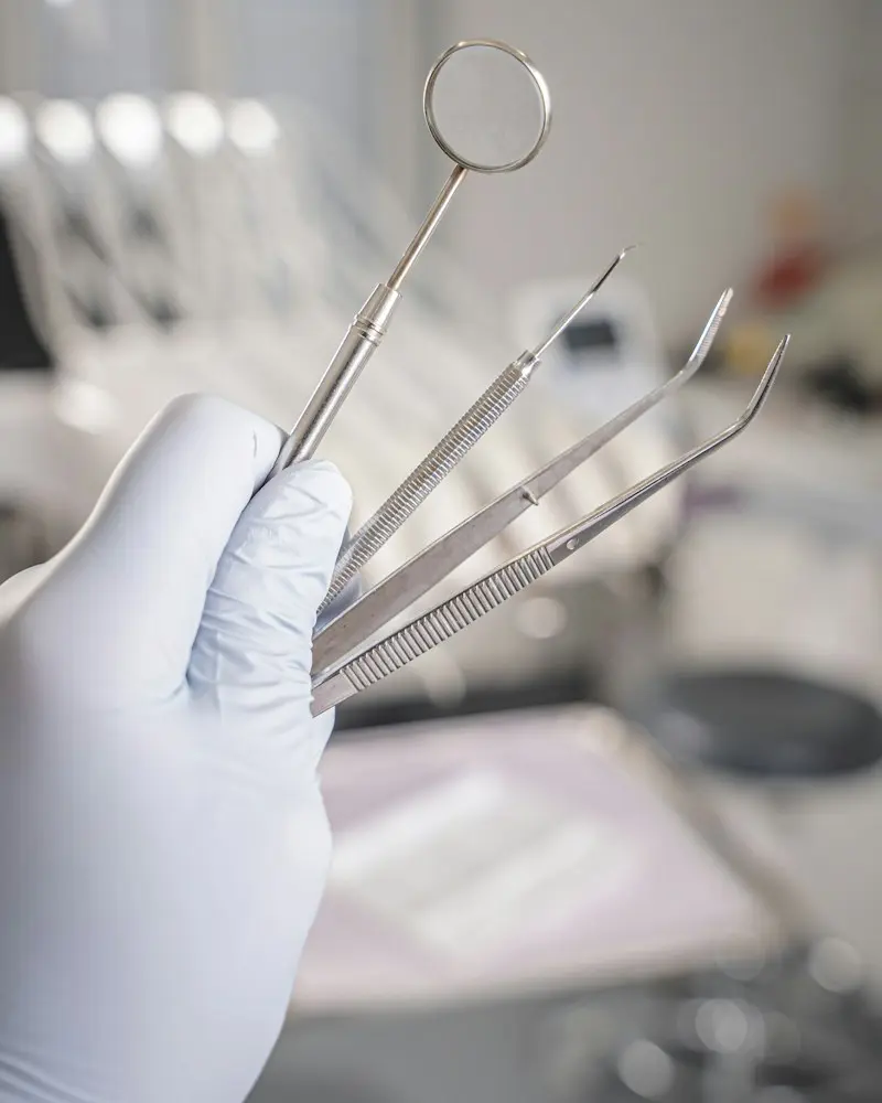 A gloved hand holding a dental mirror and probes