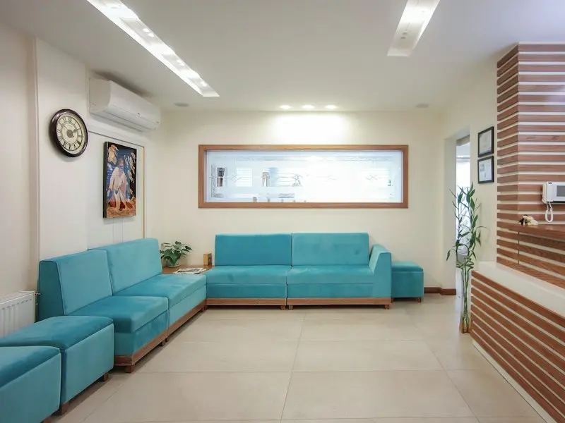 Waiting area with teal sofas, a wall clock and a reception window